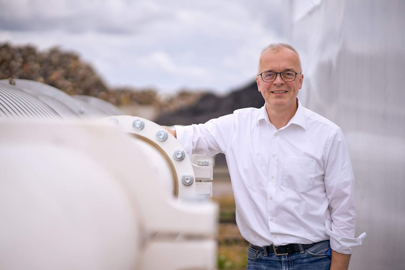 Porträt eines Mannes im weissen Hemd zeigt ihn in einem technischen Umfeld mit weissen Röhren unter freiem Himmel. environmental portrait,Sachverstand fotografisch visualisiert